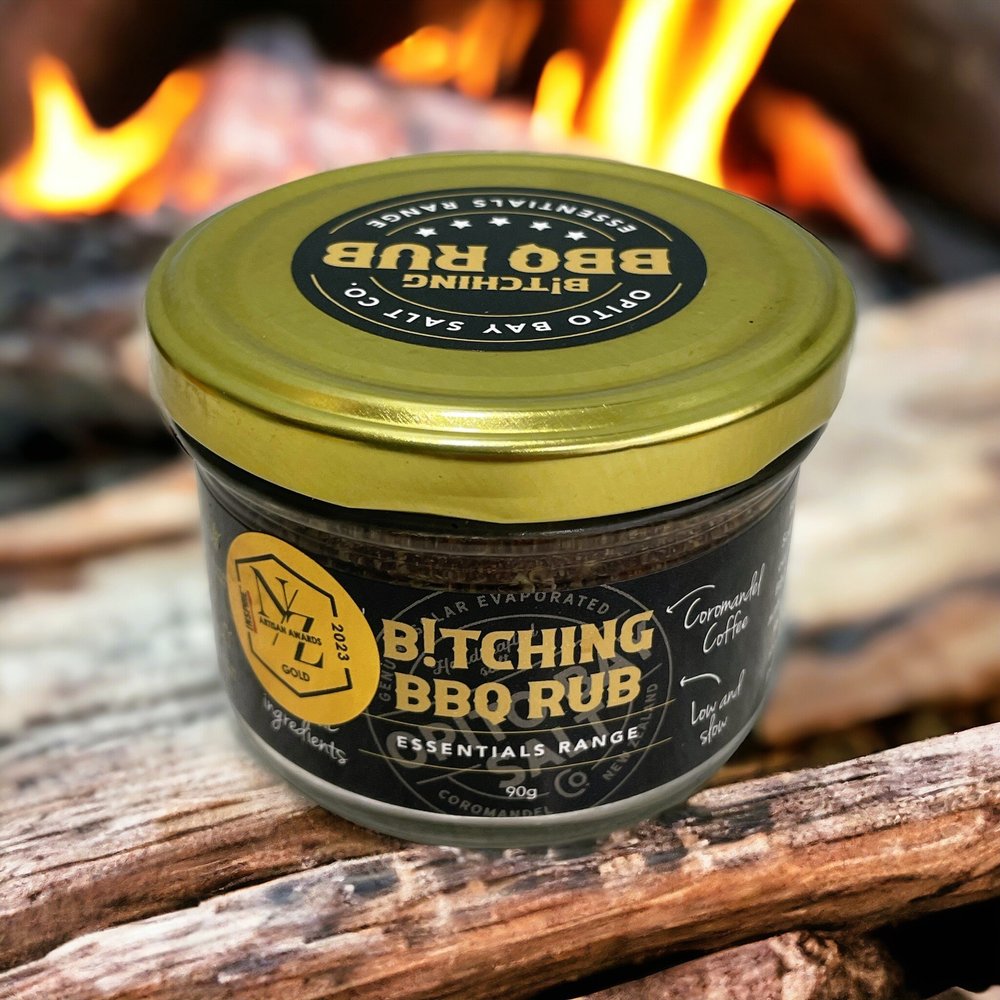 Jar of BBQ rub with a gold lid on wooden logs with flames in the background