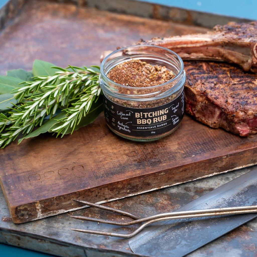 Jar of BBQ rub on a wooden cutting board with ribs and rosemary