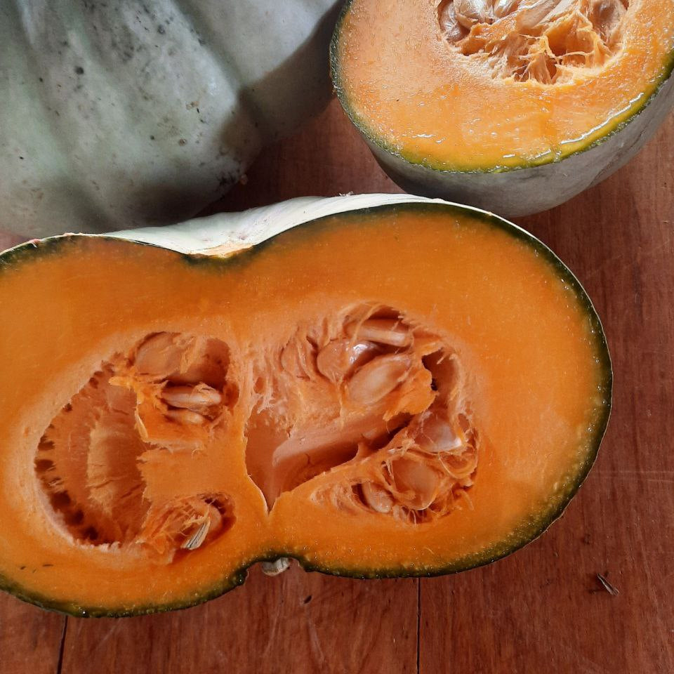 Halved pumpkin on a wooden surface with a whole pumpkin in the background.