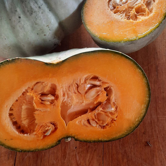 Halved pumpkin on a wooden surface with a whole pumpkin in the background.